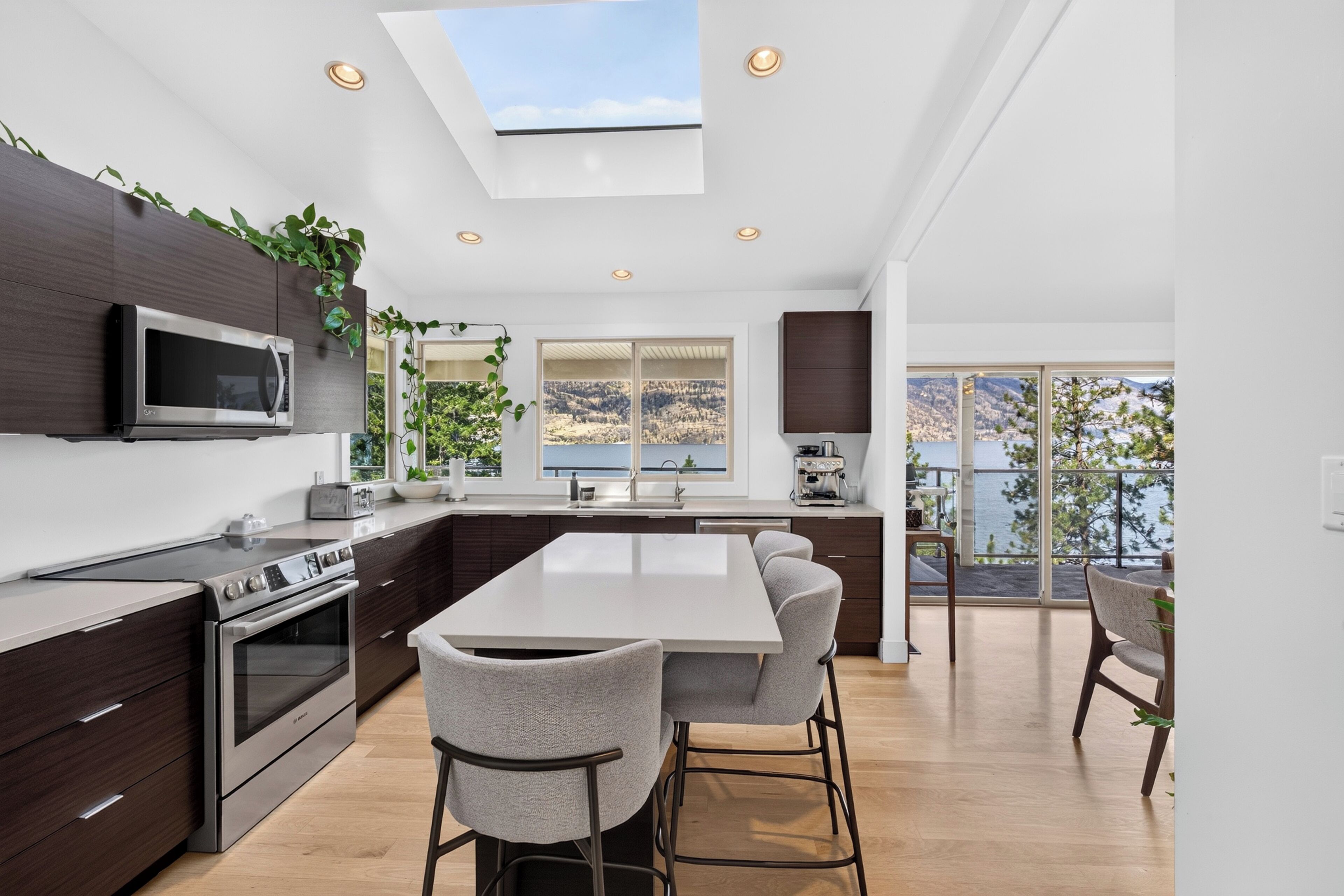 A modern kitchen with a central island, dark cabinetry, stainless steel appliances, and a skylight.