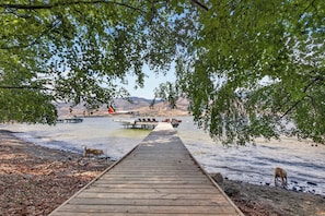 A wooden dock leading to a lake with a boat docked on the shore. - Lakefront Luxury on Okanagan Lake | Private Beach, Dock, Hot Tub & Sauna (Kelowna)