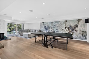 Una sala de estar moderna con una mesa de ping pong, un sofá gris y un mural grande en la pared.