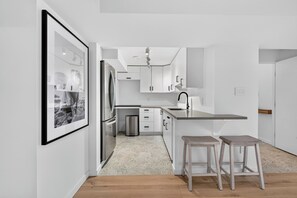 Una cocina moderna con armarios blancos, un refrigerador de acero inoxidable, un lavamanos y dos taburetes.