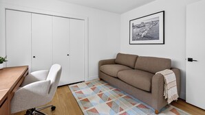 Ett rum med en vit garderob, en brun soffa, ett skrivbord med en stol och en mönstrad matta.