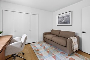 A room with a white wardrobe, a brown sofa, a desk with a chair, and a patterned rug. - Lakefront Luxury on Okanagan Lake | Private Beach, Dock, Hot Tub & Sauna (Kelowna)
