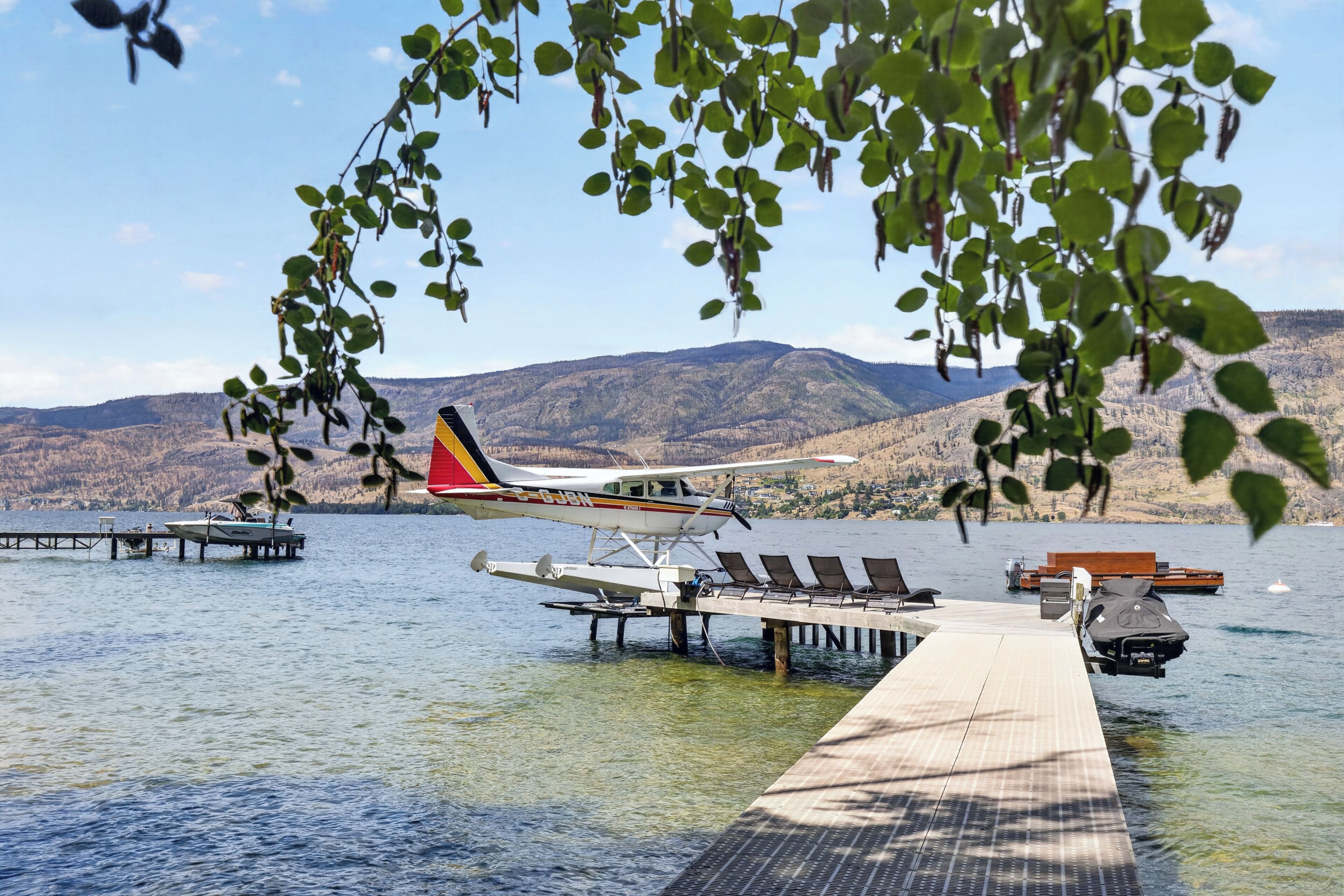 A seaplane docked at a wooden pier extending into a lake, with mountains in the background.