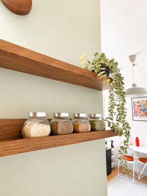 A kitchen with wooden shelves holding jars of spices and a hanging plant. - Cozy Studio in the Heart of Nantes | Everything Within Walking Distance | Train Station 5 Minutes Away (Nantes)