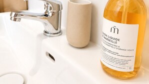 En handfat i badrummet med ett kromfärgat blandare och en beige mugg.