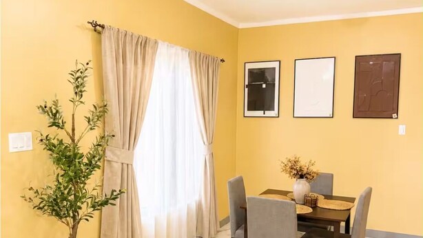A dining area with a table set for four, a potted plant, and a window with curtains. - Cozy 3-bedroom house in peaceful Kingston with AC comfort (Kingston)
