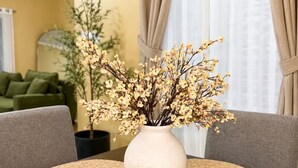 A dining table with a white vase of flowers, surrounded by woven placemats. - Cozy 3-bedroom house in peaceful Kingston with AC comfort (Kingston)