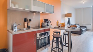Eine kompakte Küche mit modernem Design, inklusive Einbauofen, Kaffeemaschine und Toaster. Im angrenzenden Bereich befinden sich Hocker und ein Esstisch.