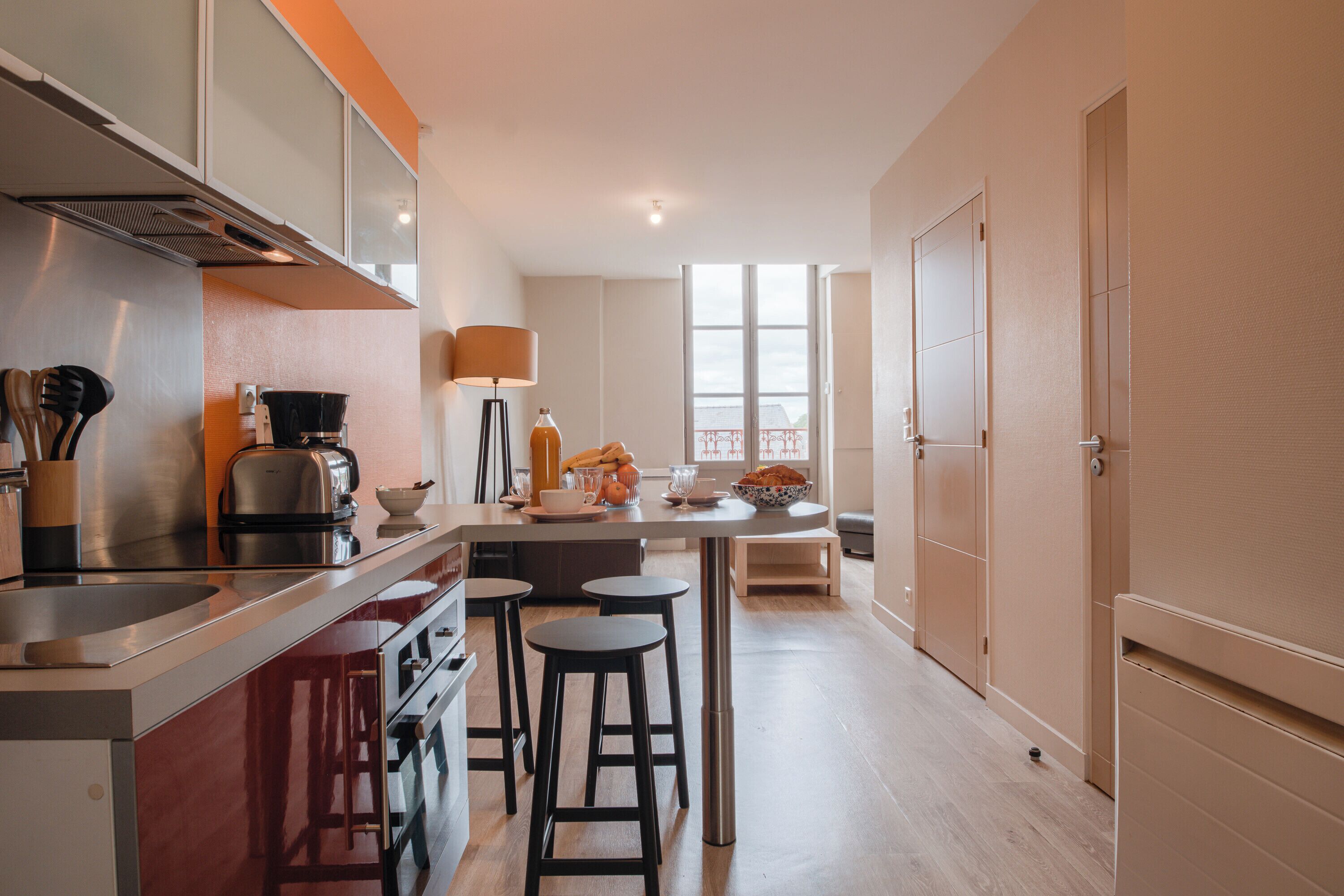 A modern kitchen with a built-in stove, a coffee maker, and a dining area with stools.