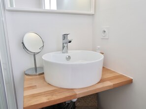 Une salle de bain avec un lavabo blanc, un miroir rond et un plan de toilette en bois.