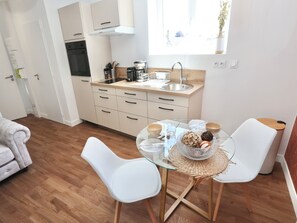 A modern kitchen with a sink, stove, and cabinets. There is a dining table with chairs and a vase with flowers on the window sill. - Le Corail - centre-ville - TV (Pontivy)