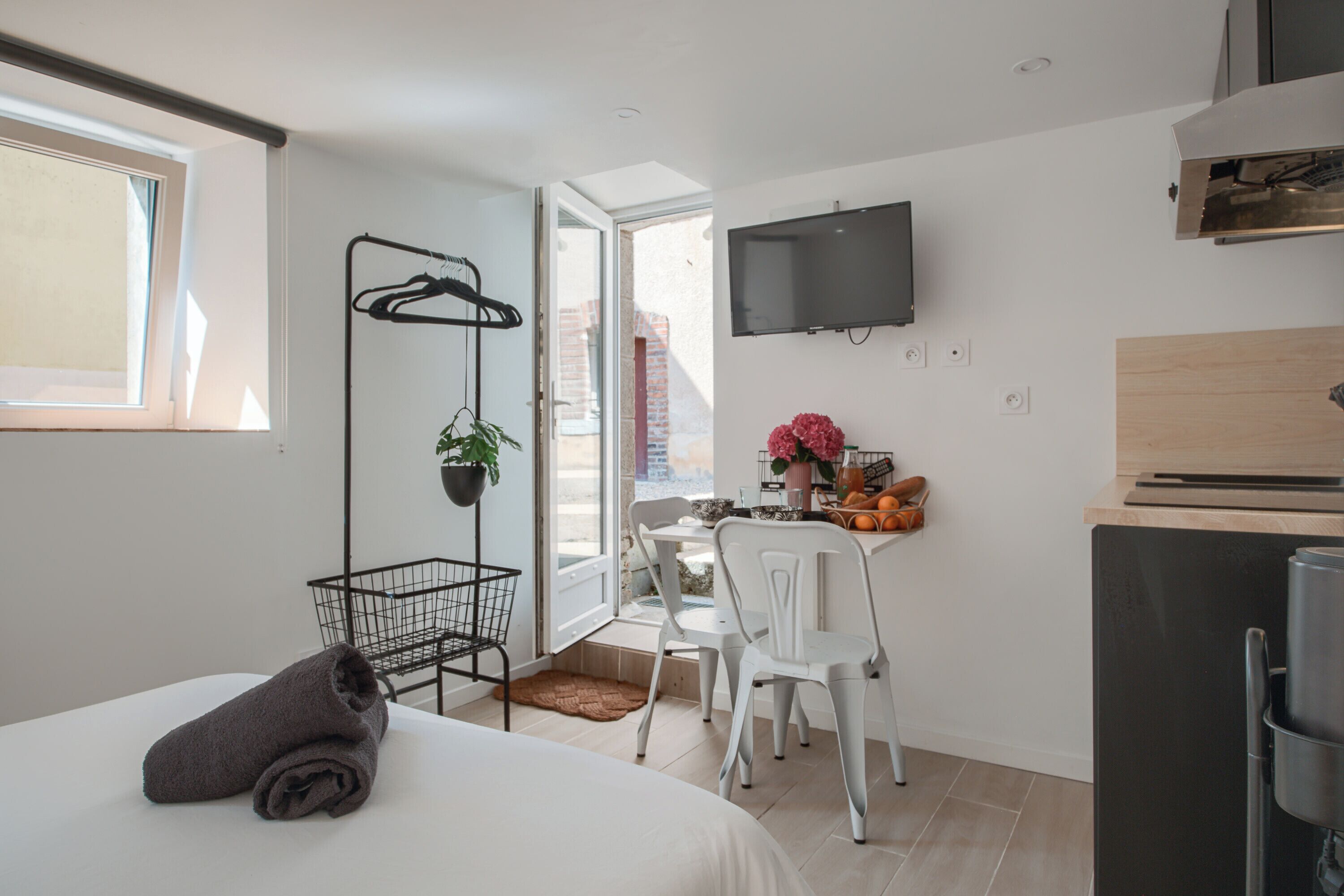 A compact hotel room with a bed, a desk, a chair, a TV, and a kitchenette.