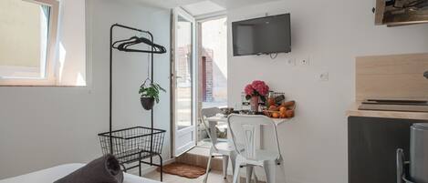 A compact hotel room with a bed, a desk, a chair, a TV, and a kitchenette.