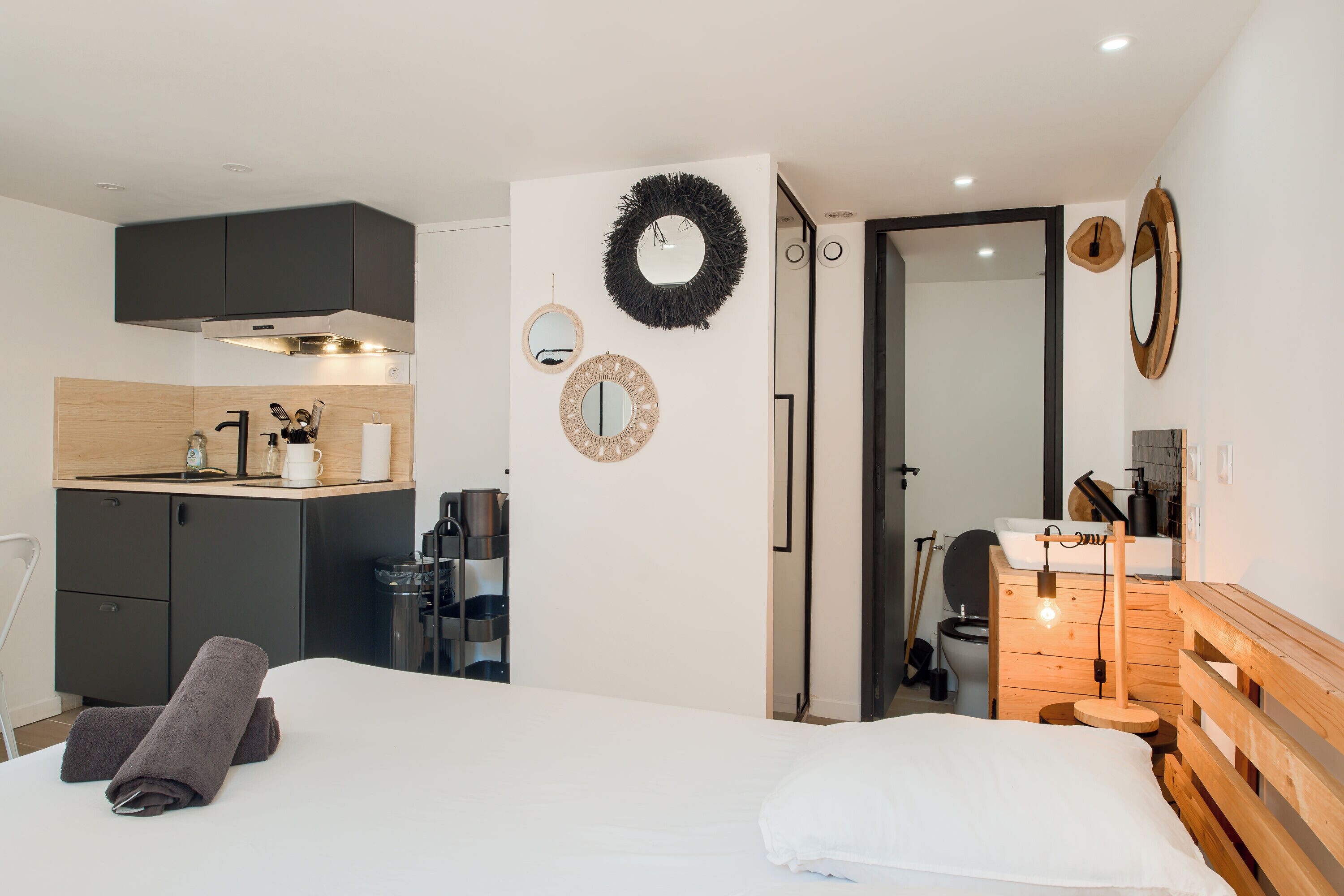 Une chambre moderne avec un lit, une tête de lit en bois, un petit banc en bois, un miroir et un luminaire fixé au mur.