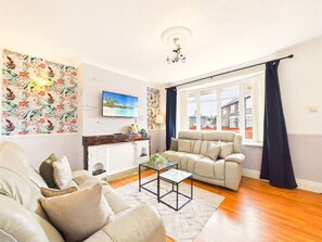 Ein Wohnzimmer mit einer Couch, einem Couchtisch, einem Kamin und einem großen Fenster mit Vorhängen.