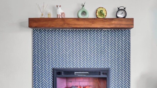 Una chimenea con un revestimiento de pared en patrón de espiga, un repisa de madera y una cesta tejida.