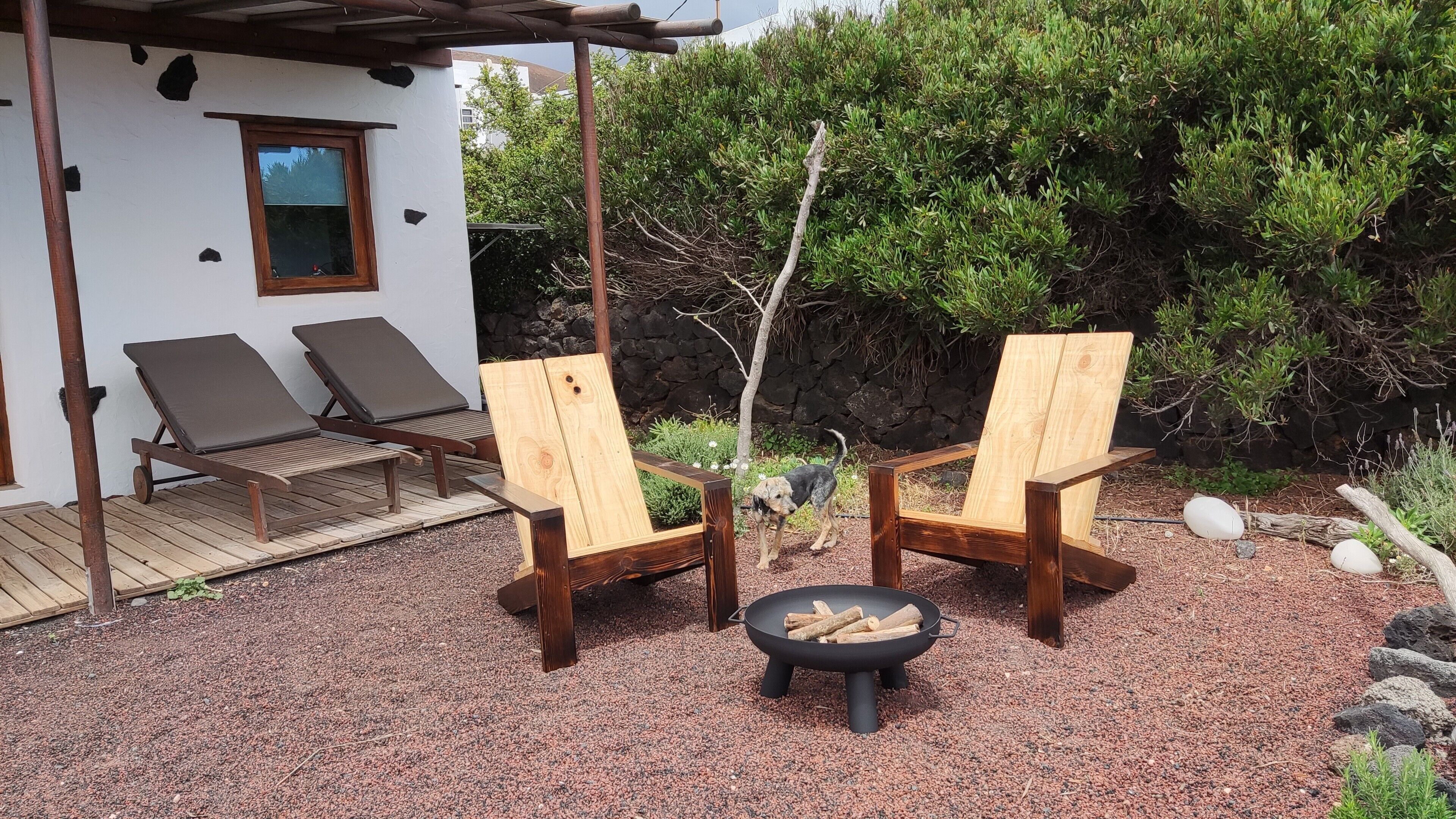 A patio with two wooden chairs, a small fire pit, and a wooden deck.