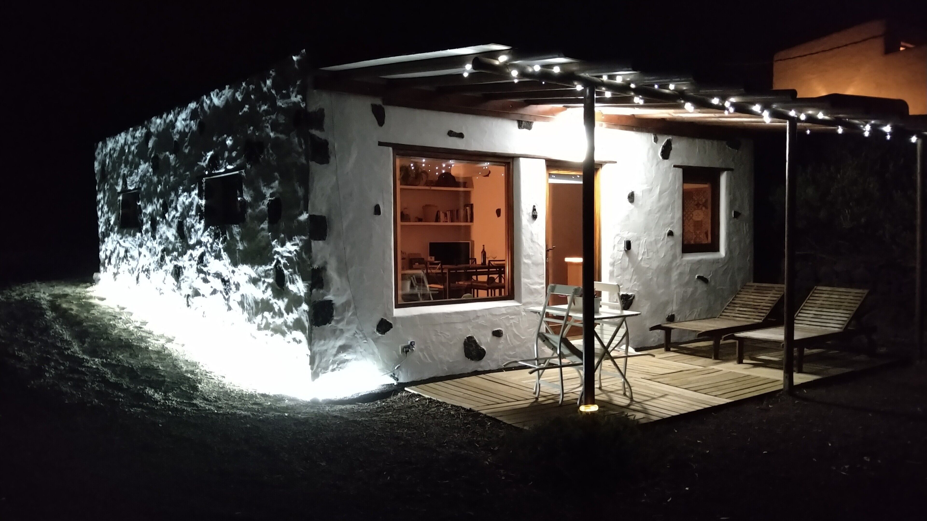 Una casa moderna con facciata in pietra, un portico coperto con posti a sedere e un interno visibile con zona pranzo.