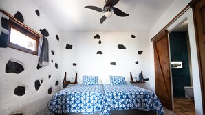 A bedroom with a bed, a ceiling fan, a window, and a door leading to a bathroom. - Sweet Tabaiba Suite - casita con vistas al mar, terraza privada y Wi-Fi (La Asomada)