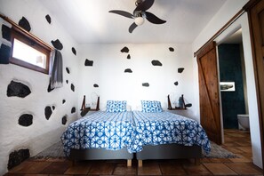 Un dormitorio con cama, ventilador de techo, ventana y puerta que da a un baño.