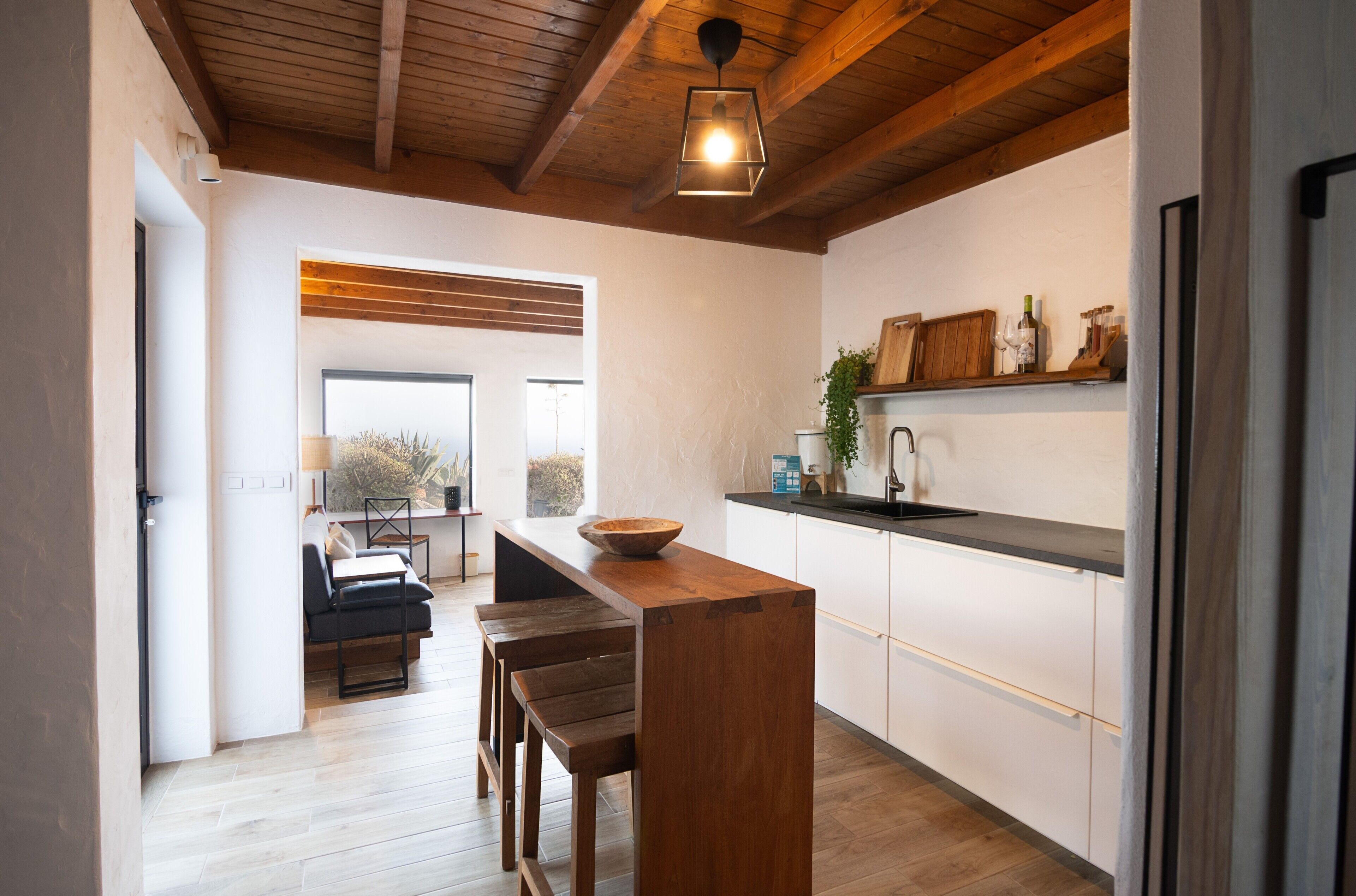 A modern kitchen with wooden beams, a central island, and a view to the outside.