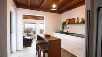 A modern kitchen with wooden beams, a central island, and a view to the outside.