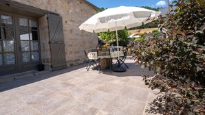 A stone building with a door and window, a table with chairs, and a white umbrella. - La Roque Vacation Rental - CANOURGUE (LA) (CANOURGUE (LA))