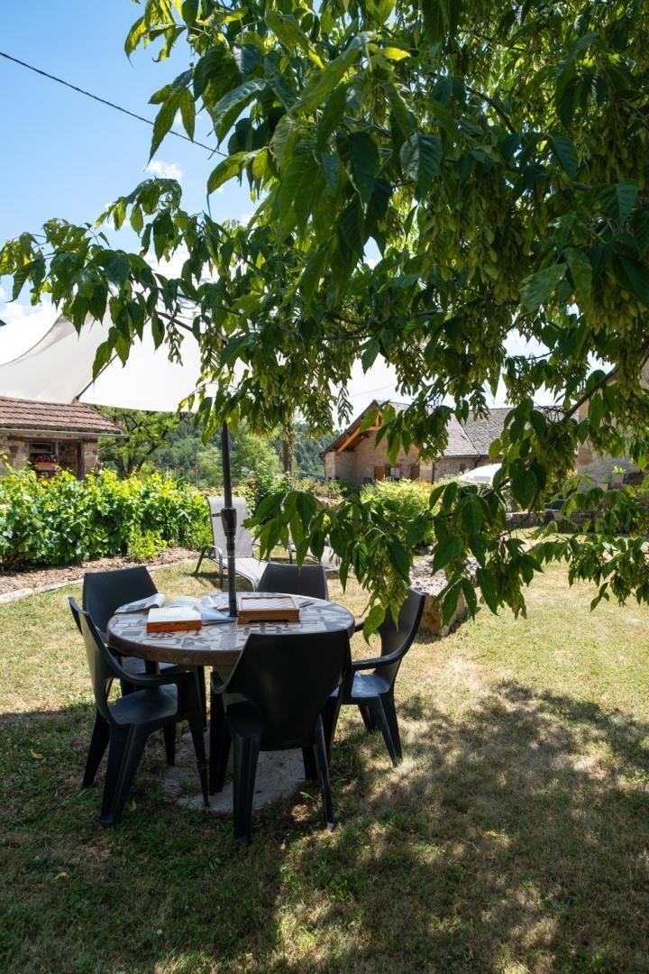 A round table with chairs under a tree, surrounded by grass and a building in the background.