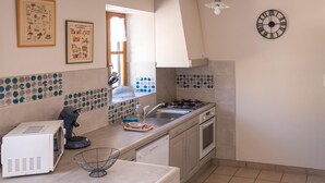A kitchen with a stove, sink, microwave, and a window with a view. - La Roque Vacation Rental - CANOURGUE (LA) (CANOURGUE (LA))