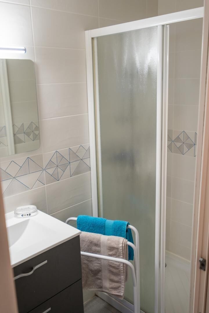 A bathroom with a shower enclosure, a towel rack with towels, and a mirror.