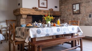 A dining area with a table set for breakfast, featuring a polka dot tablecloth, wooden chairs, and a stone fireplace in the background. - La Roque Vacation Rental - CANOURGUE (LA) (CANOURGUE (LA))