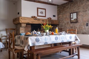 A dining area with a table set for breakfast, featuring a polka dot tablecloth, wooden chairs, and a stone fireplace in the background. - La Roque Vacation Rental - CANOURGUE (LA) (CANOURGUE (LA))