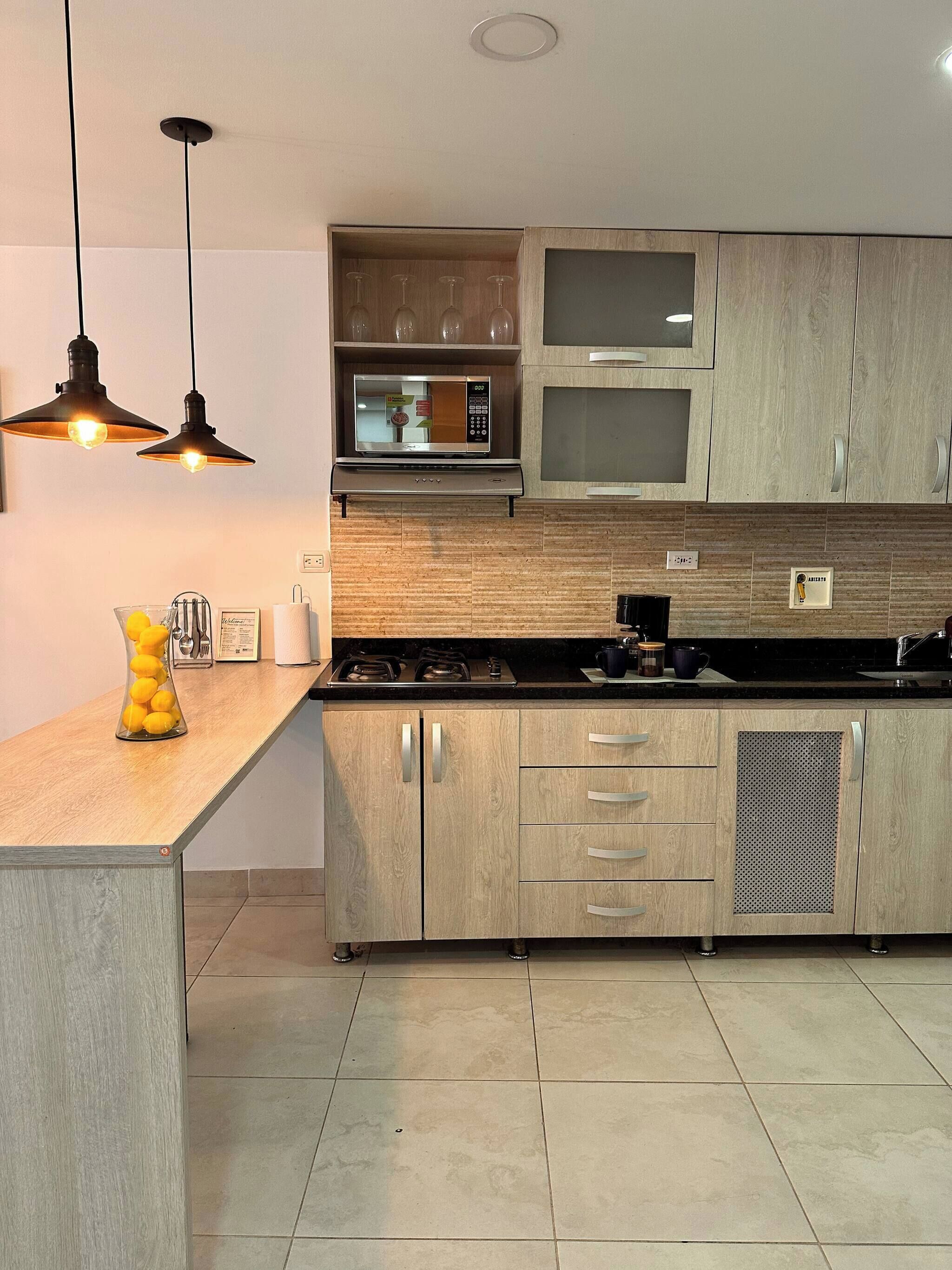 A modern kitchen with wooden cabinets, a microwave, a stove, and pendant lighting.