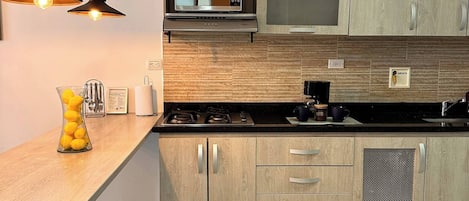 Cocina moderna con gabinetes de madera, microondas, estufa e iluminación colgante.