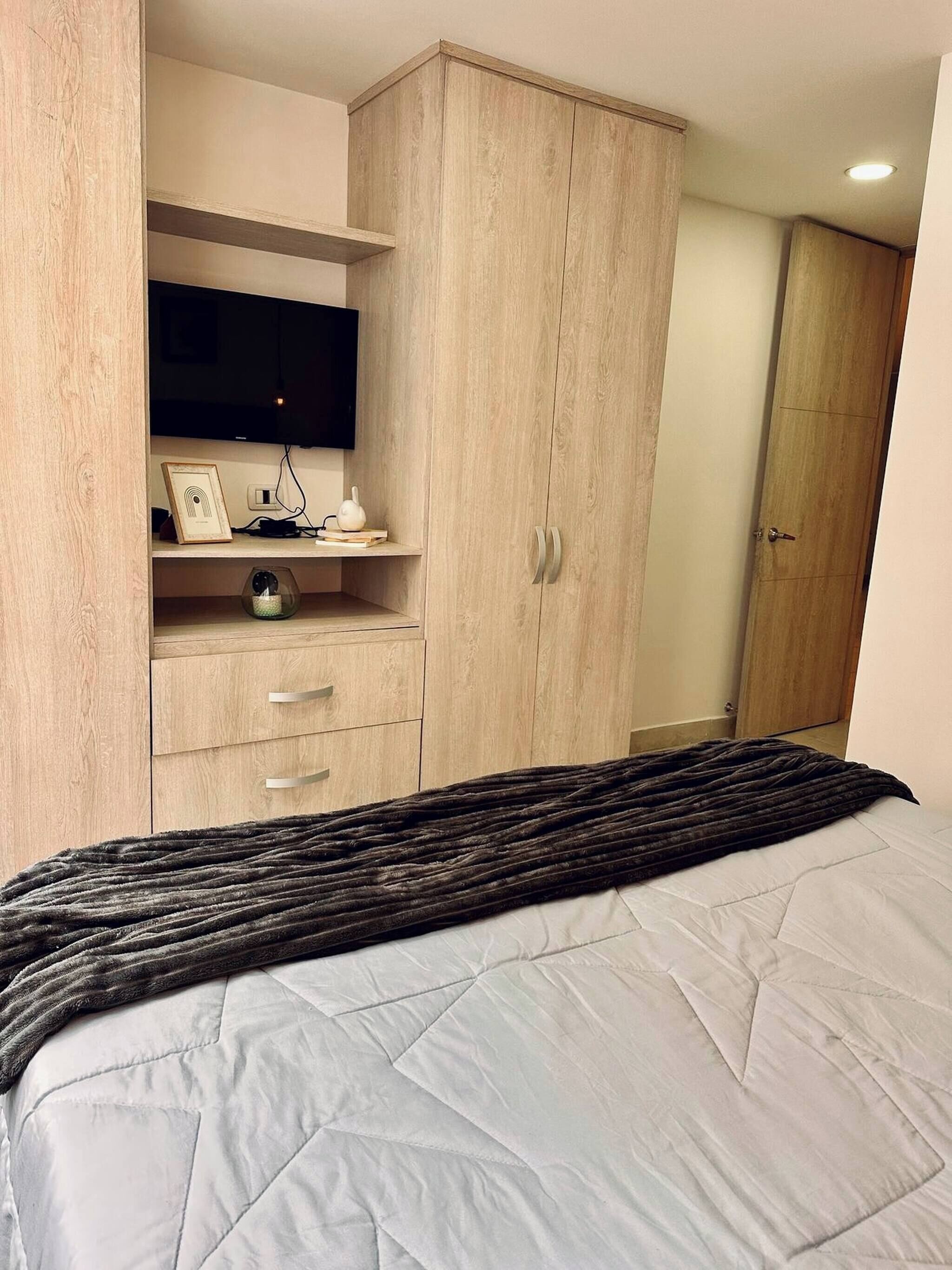 A bedroom with a bed, a wardrobe, a television, and a shelf with items.