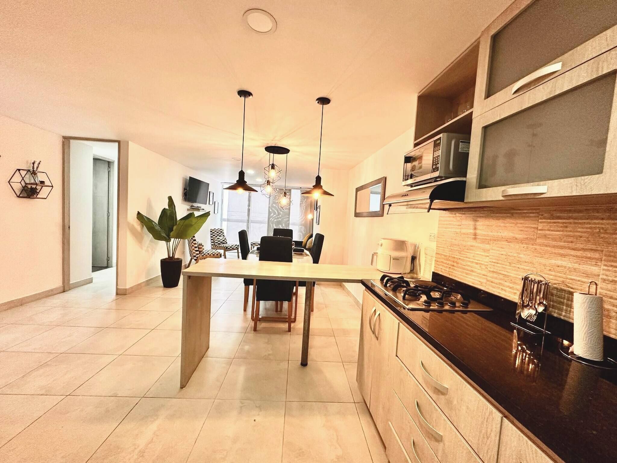 A modern kitchen with a central island, pendant lighting, and a microwave on the countertop.