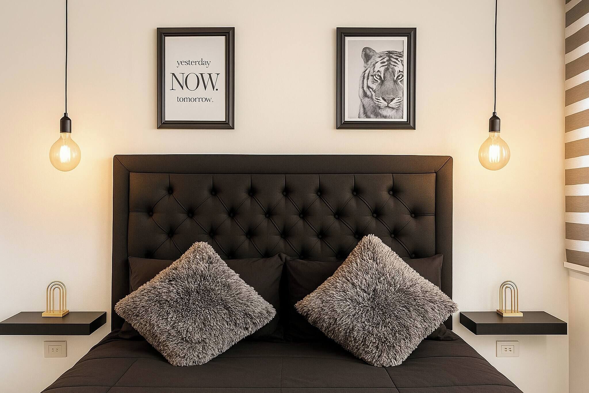 A bedroom with a tufted headboard, two fluffy pillows, a framed tiger picture, and two light bulbs.