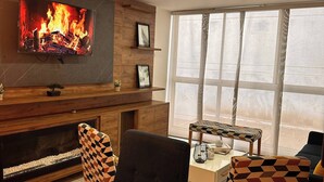 Ein modernes Wohnzimmer mit Kamin, Wand-Fernseher und Essbereich mit gemusterten Stühlen.