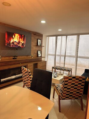 A modern living room with a fireplace, a television mounted on the wall, and a dining area with patterned chairs. - Envigado Comfortable Modern · Wifi 300 MB · Metro (Envigado)