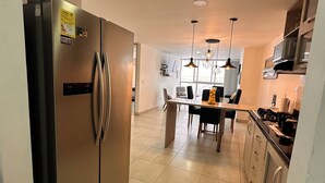 Eine moderne Küche mit einem Edelstahl-Kühlschrank, einem Esstisch mit Stühlen, Pendelleuchten und einem an der Wand befestigten Fernseher.