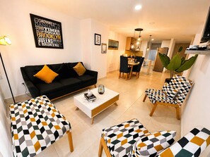 A living room with a black sofa, patterned armchairs, a coffee table, and a dining area with a wooden table and chairs. - Envigado Comfortable Modern · Wifi 300 MB · Metro (Envigado)