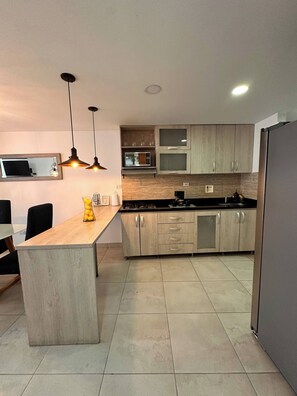 Una cocina moderna con una isla central, armarios de madera, un microondas y un refrigerador.