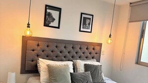 Ein Schlafzimmer mit einer gesteppten Kopfteil, einem Bett mit vielen Kissen, einem Nachttisch mit einer Lampe und zwei Wandleuchten.