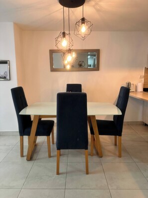 A dining area with a white table, four dark chairs, and a geometric pendant light fixture. - Envigado Comfortable Modern · Wifi 300 MB · Metro (Envigado)