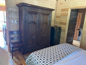 A bedroom with a wooden wardrobe, a bed with a checkered bedspread, and a chair.