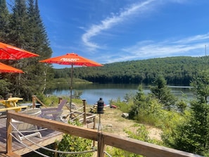 A lakeside deck with outdoor seating and a view of a lake surrounded by forest.