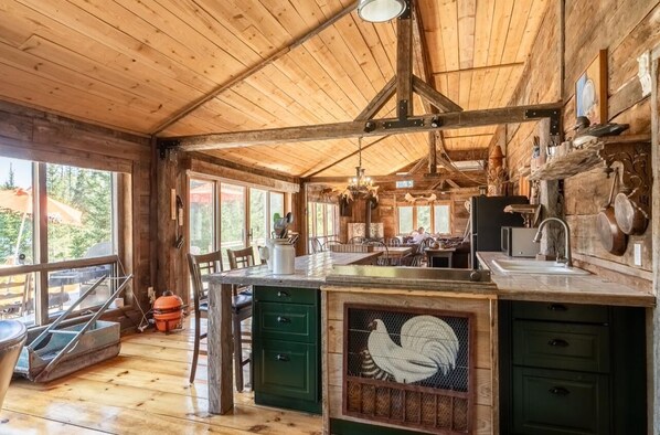 A rustic wooden interior with a large kitchen island, wooden beams, and a view through large windows.