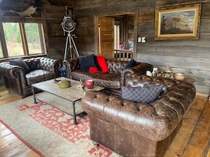 A rustic cabin interior with leather sofas, a tripod-mounted telescope, and a framed painting on the wall.