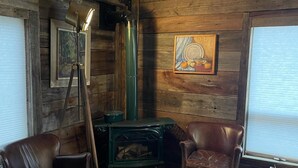 A rustic room with wooden walls, a green stove, two leather chairs, a framed painting, and a cowhide rug. - Beautifully Private Chalet in Sainte Anne du Lac! Perfect lake! (Sainte Anne du Lac)