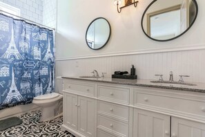 Une salle de bain avec un meuble-lavabo blanc, deux vasques, des toilettes et un rideau de douche orné de motifs sur le thème de Paris.